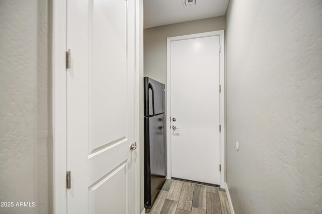 corridor featuring a textured wall, visible vents, and light wood-style floors