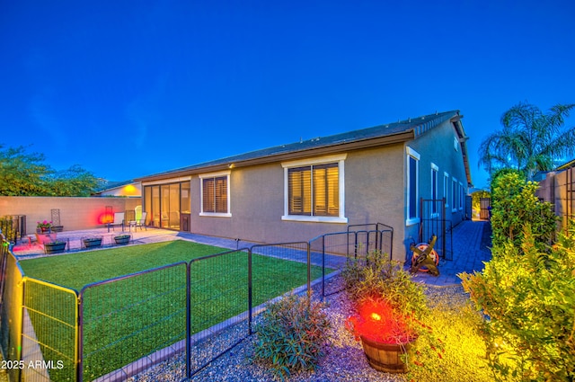 back of house with a fenced backyard, stucco siding, a yard, and a patio area