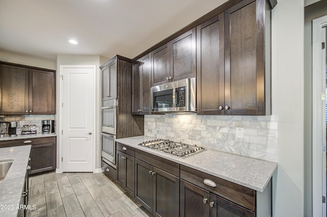 kitchen with light stone countertops, decorative backsplash, dark brown cabinets, and stainless steel appliances