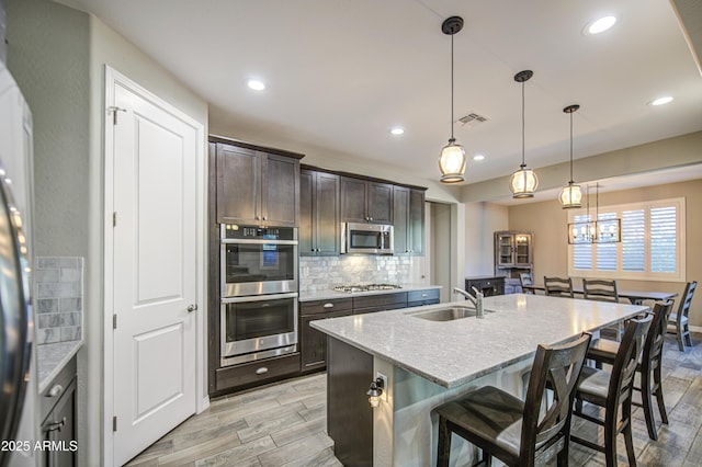kitchen featuring dark brown cabinetry, visible vents, appliances with stainless steel finishes, tasteful backsplash, and a sink