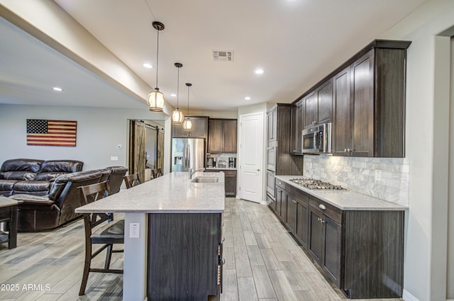 kitchen featuring dark brown cabinetry, a breakfast bar, open floor plan, backsplash, and stainless steel appliances