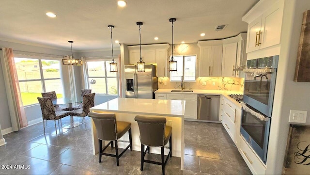 kitchen featuring tasteful backsplash, stainless steel appliances, white cabinets, sink, and pendant lighting