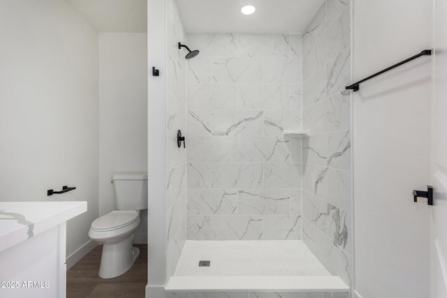 bathroom with hardwood / wood-style floors, tiled shower, toilet, and vanity