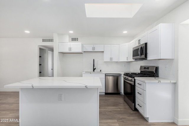 kitchen with appliances with stainless steel finishes, sink, white cabinetry, light stone counters, and a kitchen island