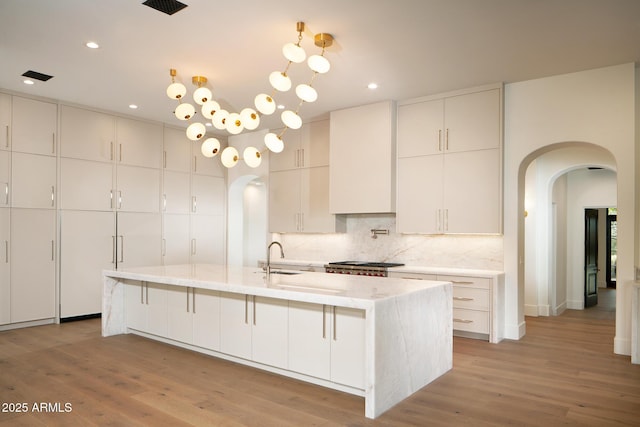 kitchen featuring light wood-type flooring, decorative backsplash, arched walkways, and a sink