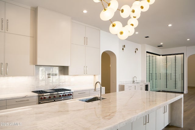 kitchen with a sink, double oven range, arched walkways, and decorative backsplash