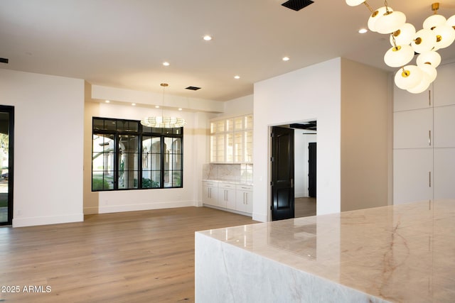 interior space featuring light stone counters, decorative backsplash, an inviting chandelier, and light wood-style flooring