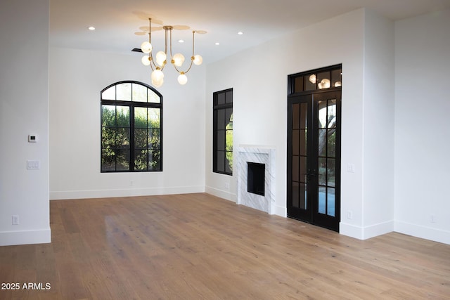 unfurnished living room featuring wood finished floors, baseboards, recessed lighting, a high end fireplace, and a notable chandelier