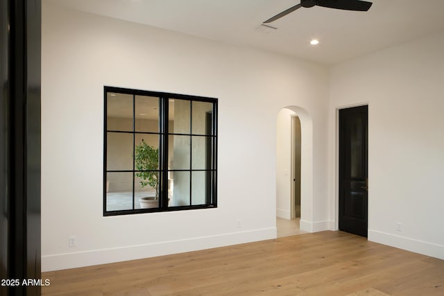 unfurnished room featuring baseboards, arched walkways, light wood finished floors, and ceiling fan