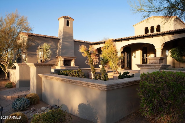 mediterranean / spanish-style home featuring a tile roof, stucco siding, and a lit fireplace