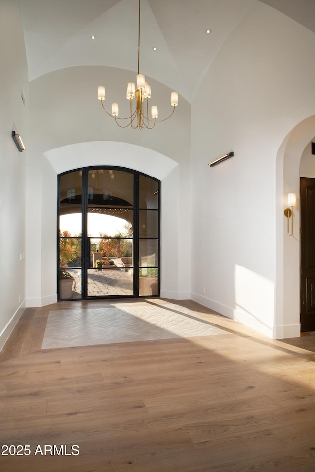 foyer entrance with arched walkways, high vaulted ceiling, baseboards, and wood finished floors