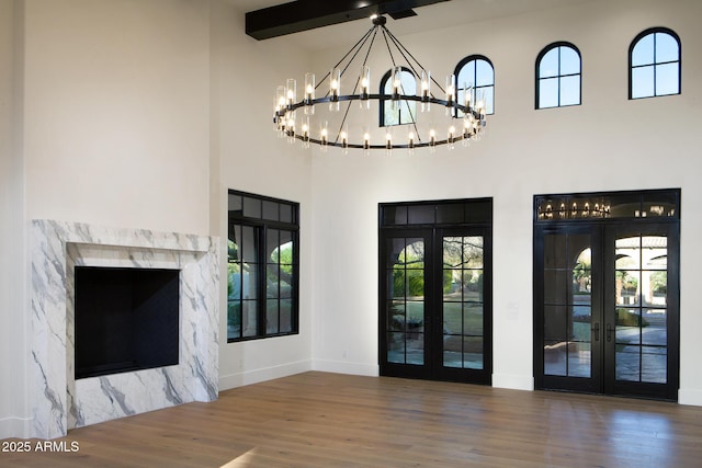 unfurnished living room featuring a chandelier, french doors, a high ceiling, and wood finished floors