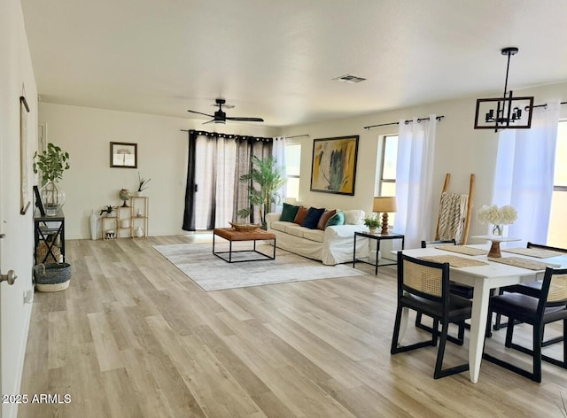 living area with visible vents, light wood finished floors, and ceiling fan with notable chandelier
