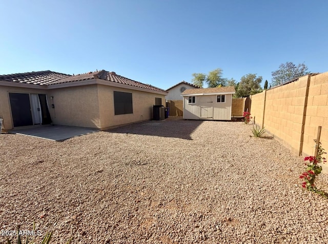 back of property with a storage shed, central air condition unit, an outdoor structure, a fenced backyard, and stucco siding