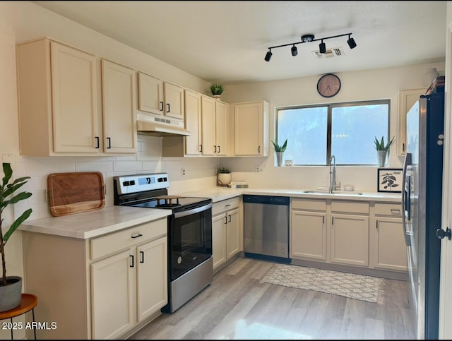 kitchen with backsplash, appliances with stainless steel finishes, light wood-type flooring, a sink, and under cabinet range hood