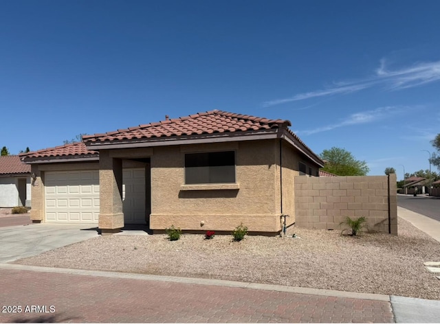 view of front of property featuring driveway, a tile roof, a garage, fence, and stucco siding