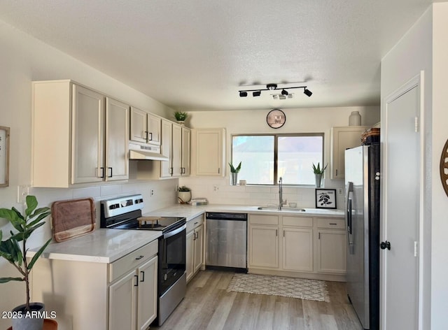 kitchen featuring light wood-type flooring, light countertops, under cabinet range hood, a sink, and appliances with stainless steel finishes
