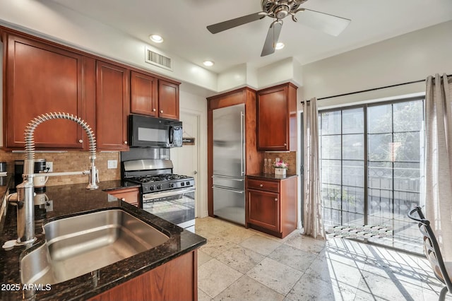 kitchen with visible vents, decorative backsplash, appliances with stainless steel finishes, a sink, and dark stone countertops