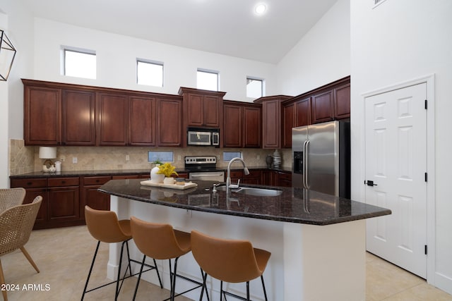 kitchen with backsplash, a center island with sink, sink, appliances with stainless steel finishes, and high vaulted ceiling