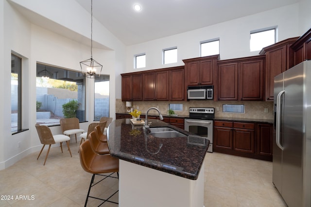 kitchen featuring decorative backsplash, a center island with sink, appliances with stainless steel finishes, high vaulted ceiling, and sink