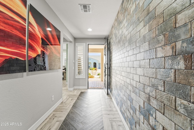 corridor with light parquet floors, brick wall, and a textured ceiling