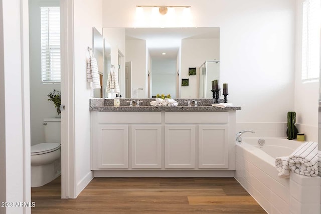 bathroom with a garden tub, toilet, wood finished floors, a shower stall, and double vanity