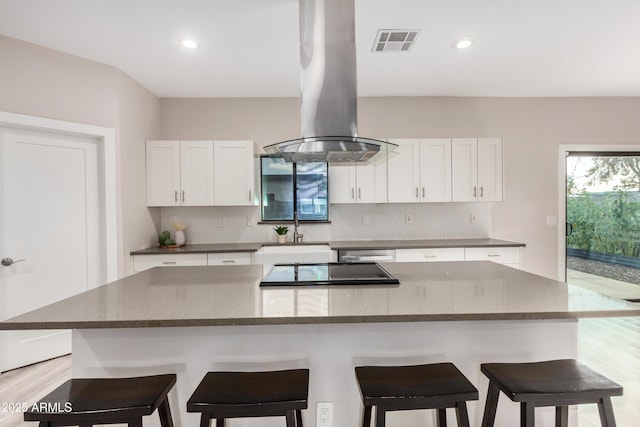 kitchen with tasteful backsplash, island exhaust hood, visible vents, and a sink