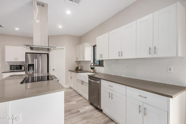 kitchen featuring island exhaust hood, stainless steel appliances, white cabinetry, a sink, and a kitchen island