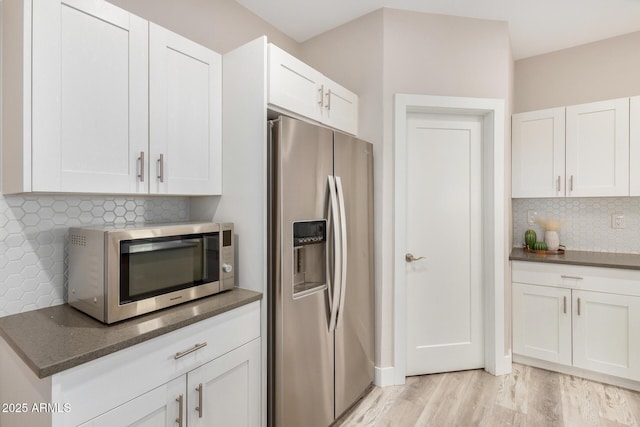 kitchen with white cabinets, decorative backsplash, dark stone counters, light wood-style flooring, and appliances with stainless steel finishes