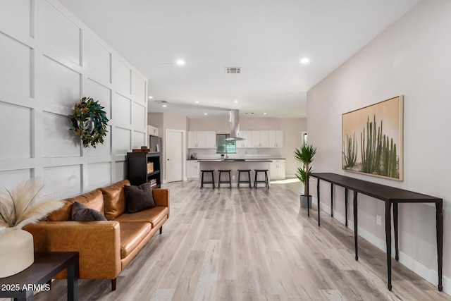 living room featuring baseboards, visible vents, a decorative wall, and light wood finished floors