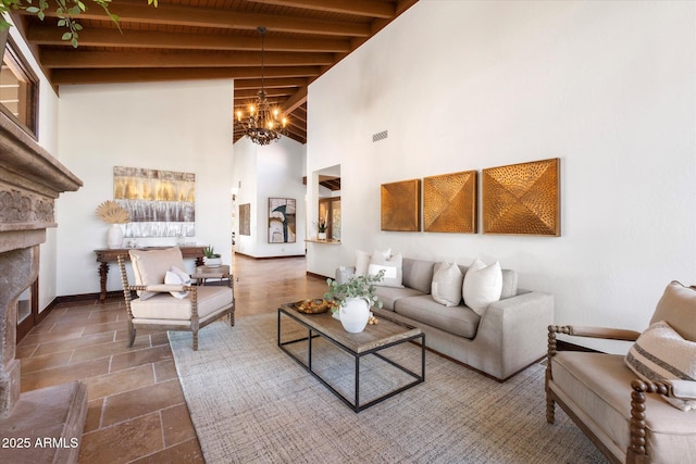 living area with baseboards, a high ceiling, a glass covered fireplace, beamed ceiling, and a chandelier