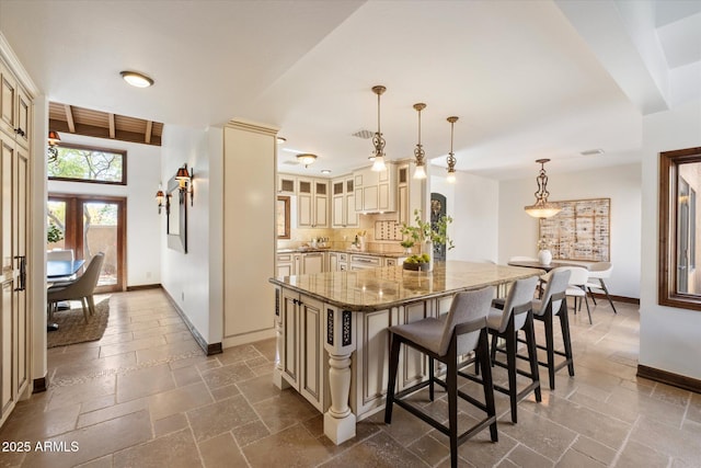 kitchen with stone tile floors, dark stone counters, cream cabinetry, glass insert cabinets, and a kitchen breakfast bar