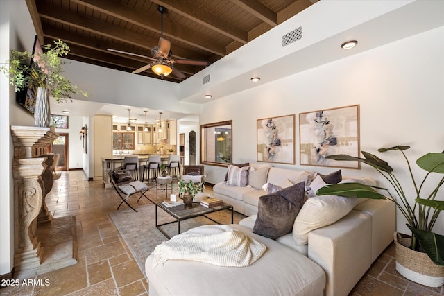 living room featuring a ceiling fan, visible vents, baseboards, stone tile flooring, and wooden ceiling