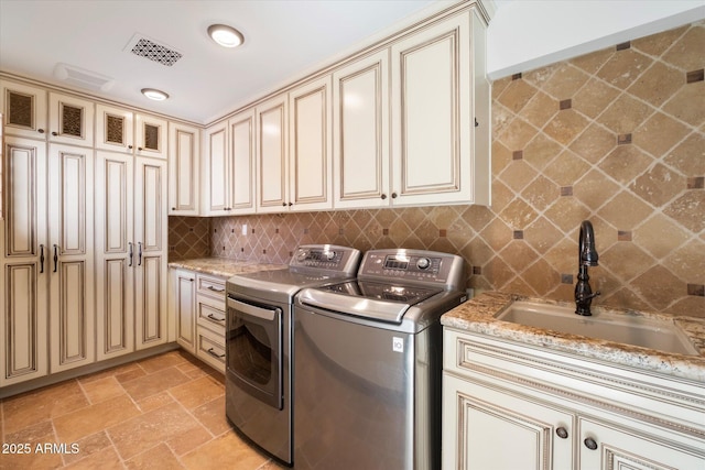 clothes washing area featuring visible vents, independent washer and dryer, a sink, stone tile flooring, and cabinet space