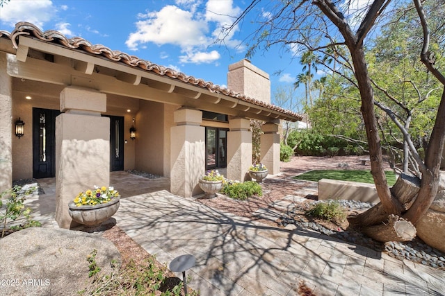 exterior space with a patio, stucco siding, a tile roof, and a chimney