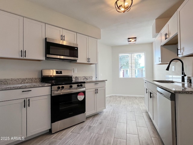 kitchen featuring stainless steel appliances, light stone countertops, sink, and white cabinets