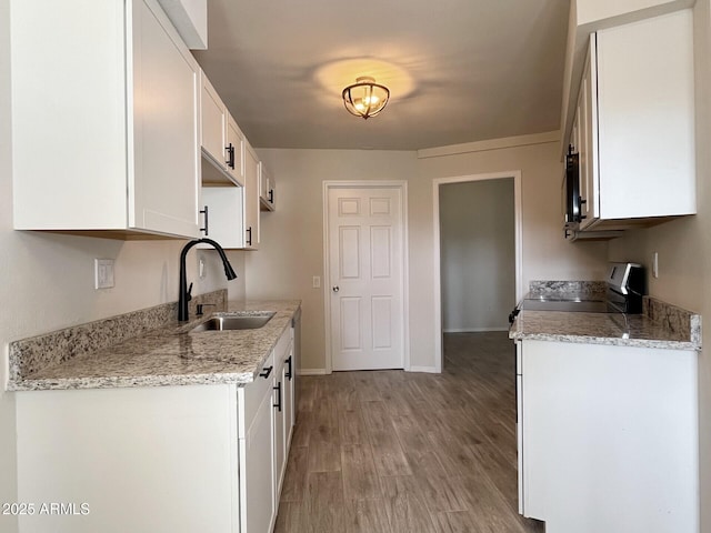 kitchen with sink, range, white cabinetry, light stone counters, and light hardwood / wood-style floors