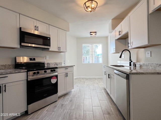 kitchen with appliances with stainless steel finishes, light stone countertops, sink, and white cabinets