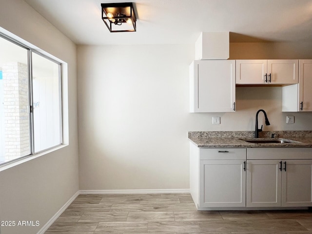 kitchen with light stone countertops, sink, white cabinets, and light wood-type flooring