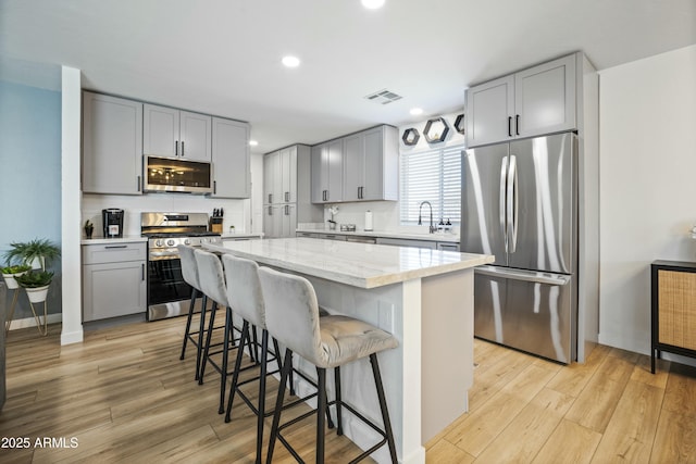 kitchen with stainless steel appliances, a center island, light stone counters, and light hardwood / wood-style floors