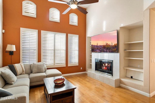 living room with built in shelves, ceiling fan, a fireplace, hardwood / wood-style floors, and a high ceiling