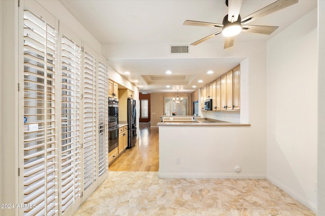 kitchen with light brown cabinetry, stainless steel refrigerator, a tray ceiling, kitchen peninsula, and ceiling fan with notable chandelier