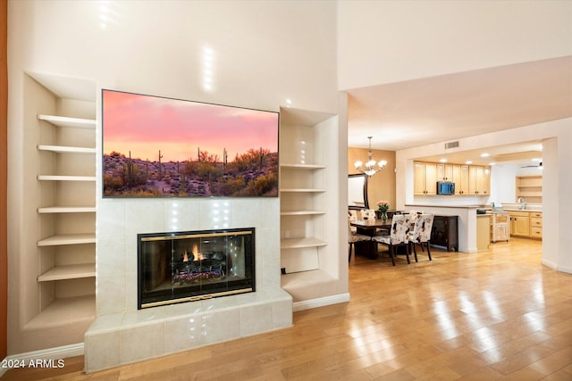 living room with sink, light hardwood / wood-style flooring, built in features, a notable chandelier, and a tiled fireplace