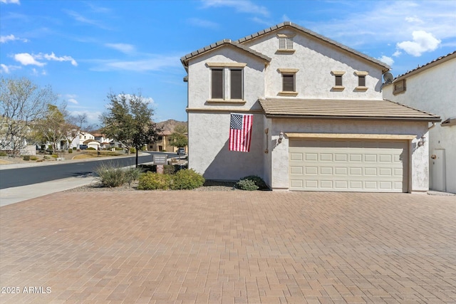 mediterranean / spanish-style house featuring a garage, a tile roof, decorative driveway, and stucco siding