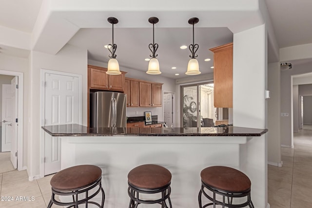 kitchen with a breakfast bar, freestanding refrigerator, dark stone countertops, and light tile patterned floors