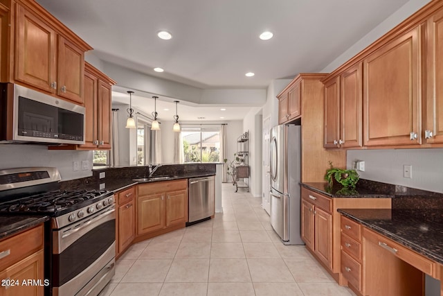 kitchen with appliances with stainless steel finishes, brown cabinets, a sink, and dark stone countertops