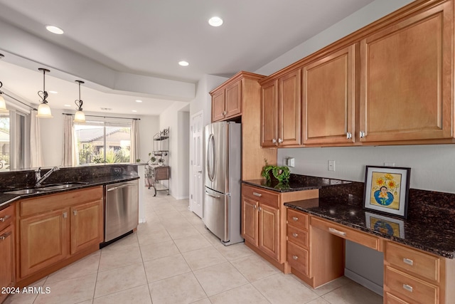 kitchen with appliances with stainless steel finishes, brown cabinets, dark stone countertops, a sink, and built in desk