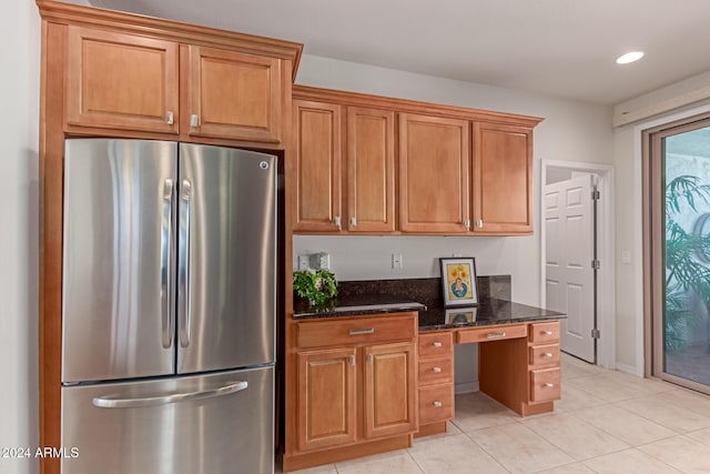 kitchen with brown cabinets, dark stone countertops, freestanding refrigerator, light tile patterned flooring, and recessed lighting