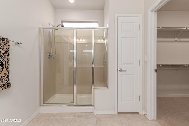 full bathroom with baseboards, a spacious closet, tile patterned flooring, and a shower stall