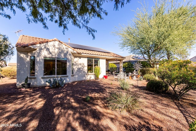 rear view of house with stucco siding, a patio, a tiled roof, and solar panels